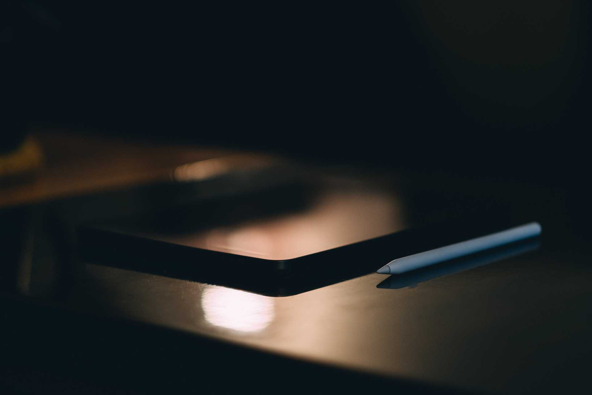 Penna bianca e un tablet appoggiati su un tavolo scuro